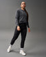 A confident individual in a gray cropped hoodie and black tapered pants stands against a muted gray background, showcasing a sporty aesthetic enhanced by white shoes and logoed socks.