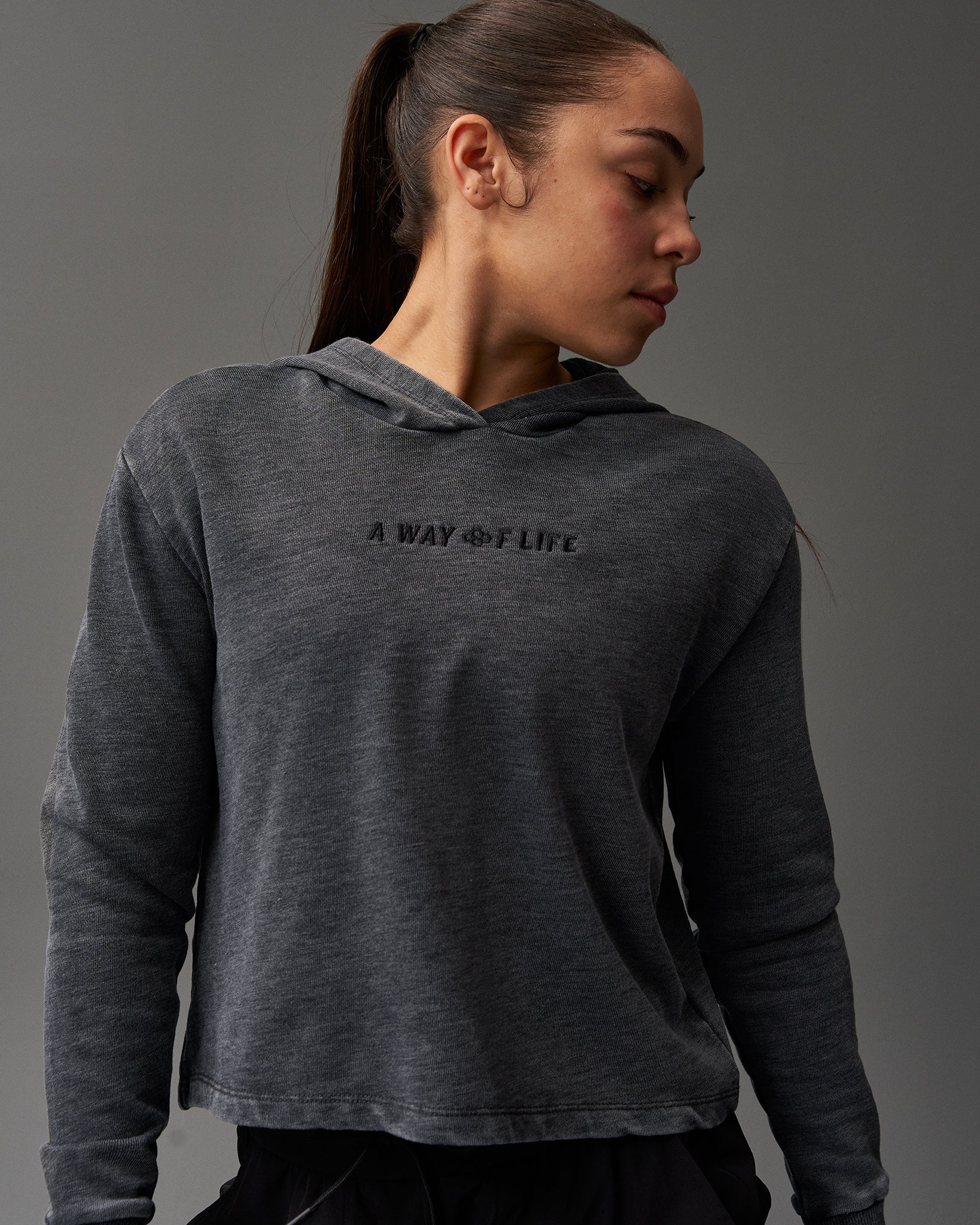 A woman in profile wears a dark gray hoodie with 'A WAY OF LIFE' embroidered on the front, set against a muted gray background, reflecting a casual and active lifestyle.