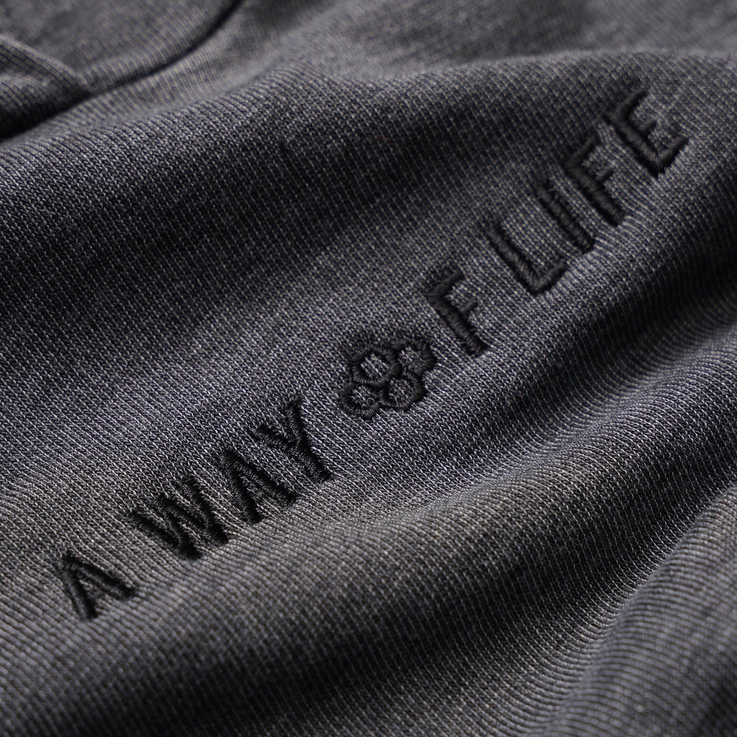 Close-up of dark gray fabric with soft texture displaying 'A WAY OF LIFE' embroidered in a modern font, highlighting a stylish aesthetic.