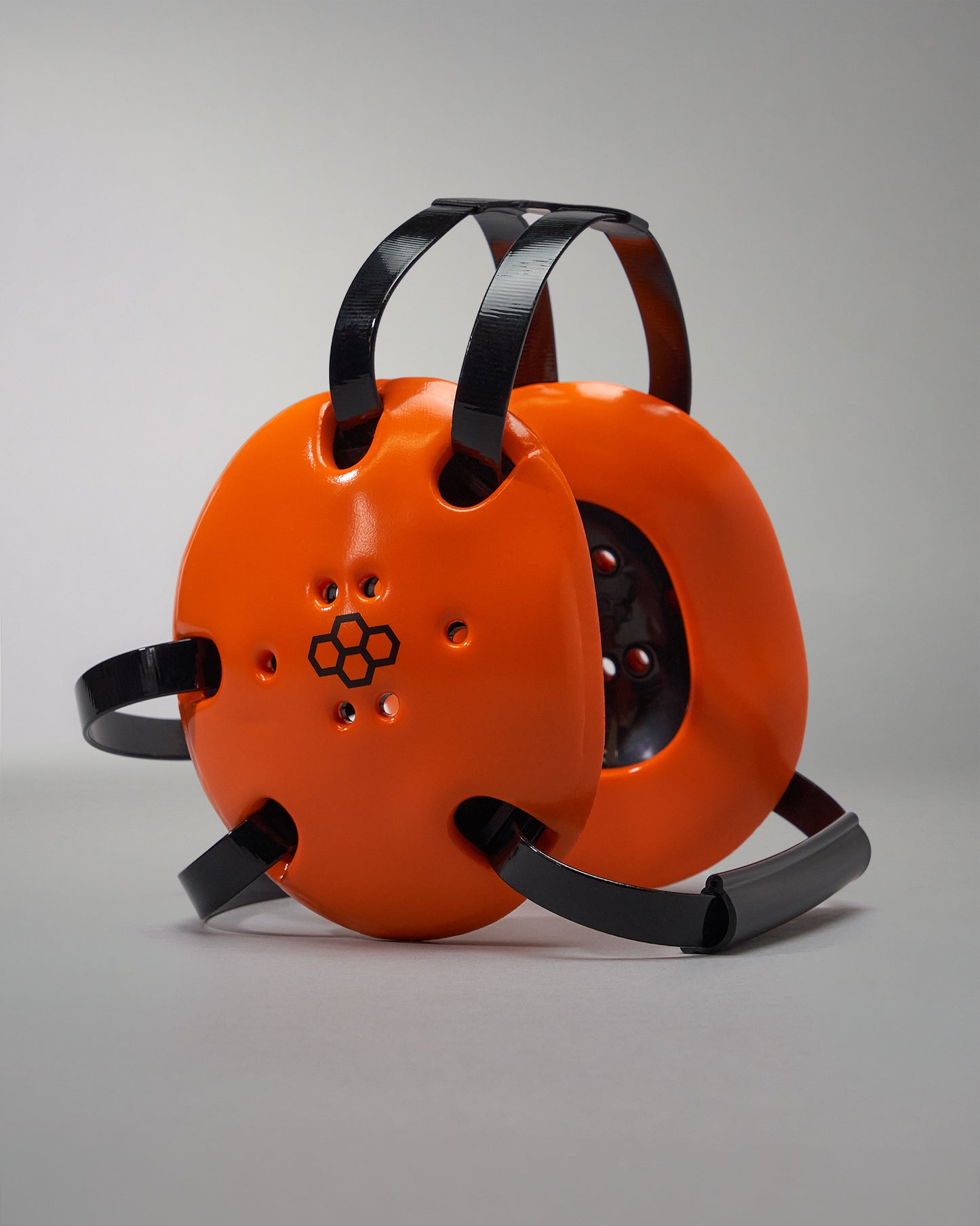 Bright orange ear protection devices with black adjustable straps and ventilation holes are set against a neutral gray background.