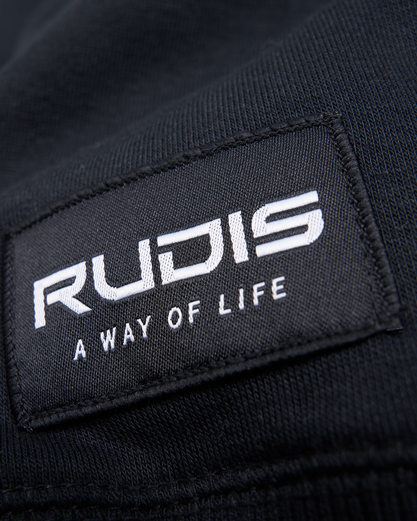 Close-up of a black fabric label featuring the brand name RUDIS and the phrase A WAY OF LIFE in white lettering