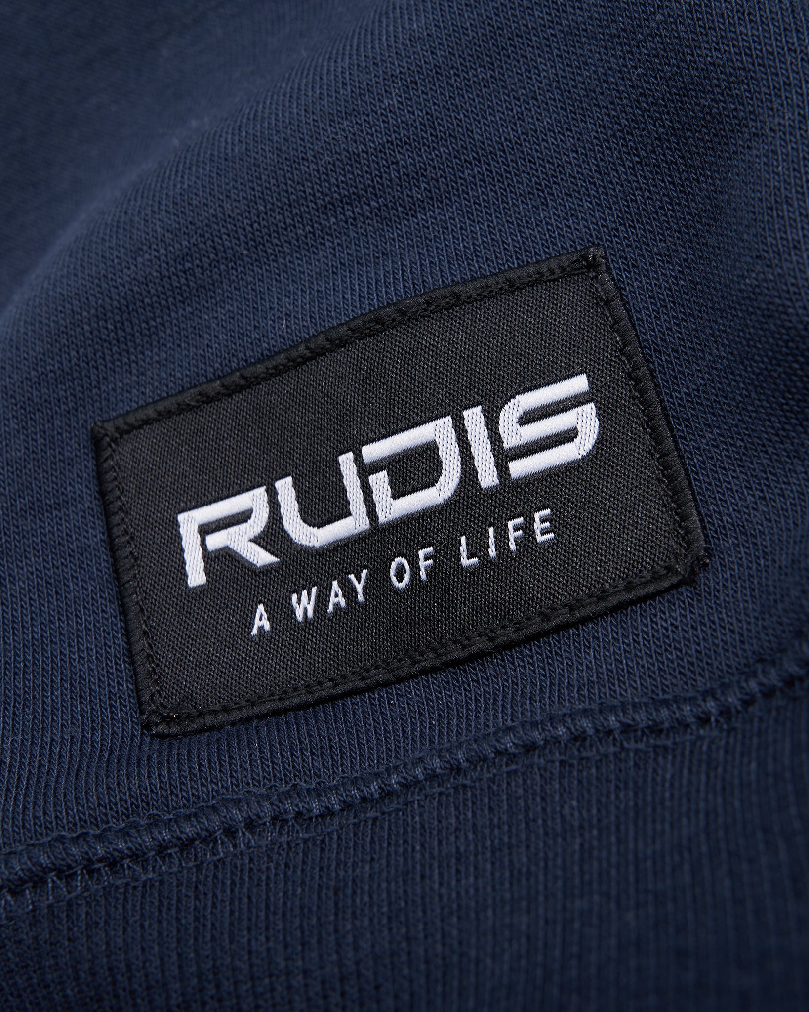 A close-up view of a fabric label featuring the brand name RUDIS and the phrase A WAY OF LIFE on a navy background