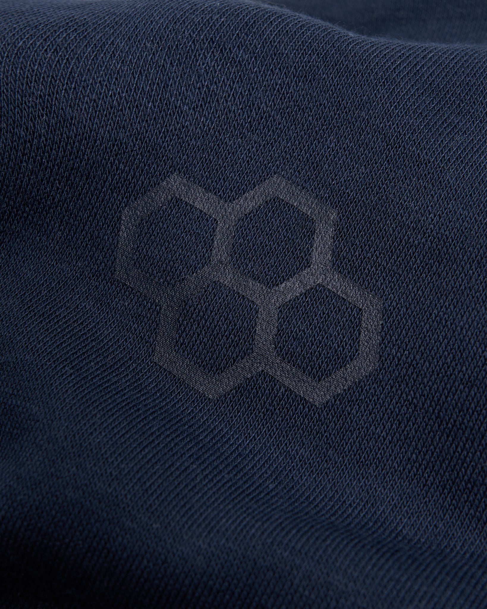 A close-up view of a dark navy fabric featuring a subtle hexagonal logo pattern highlighting its texture and design aesthetics