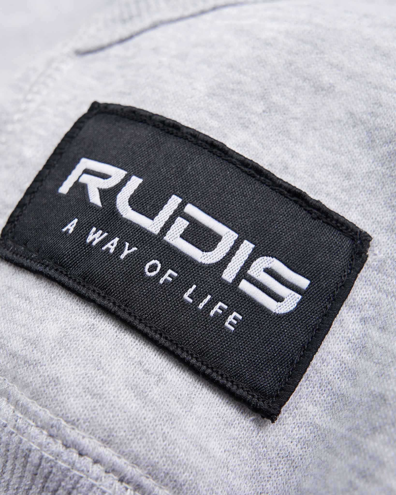 Close-up of a label featuring the brand name RUDIS and the tagline A WAY OF LIFE on a light gray fabric background