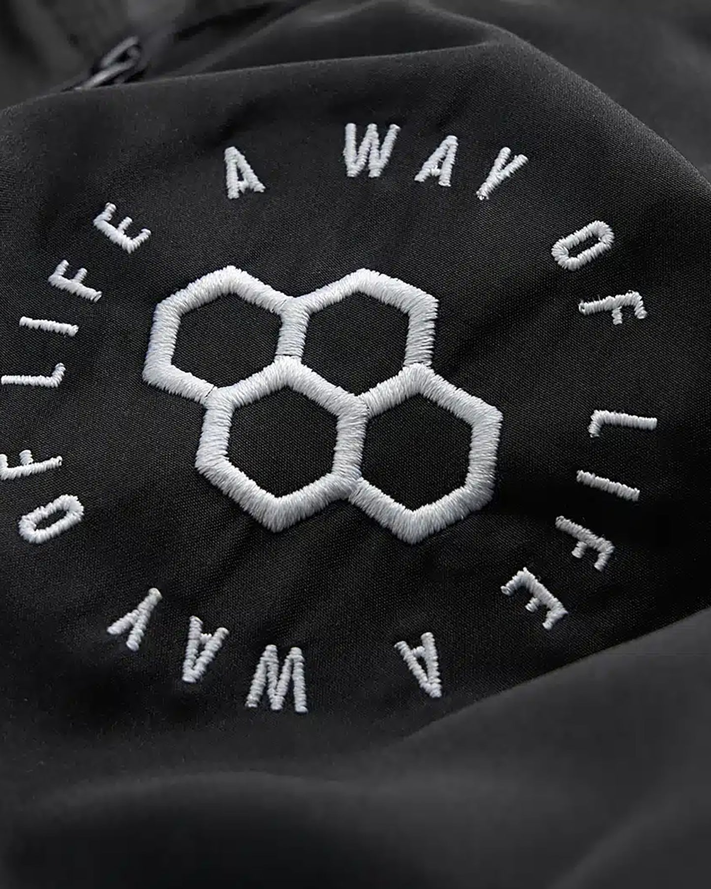 The image features an embroidered logo against a black fabric background displaying hexagonal shapes and the phrase A WAY OF LIFE in circular text