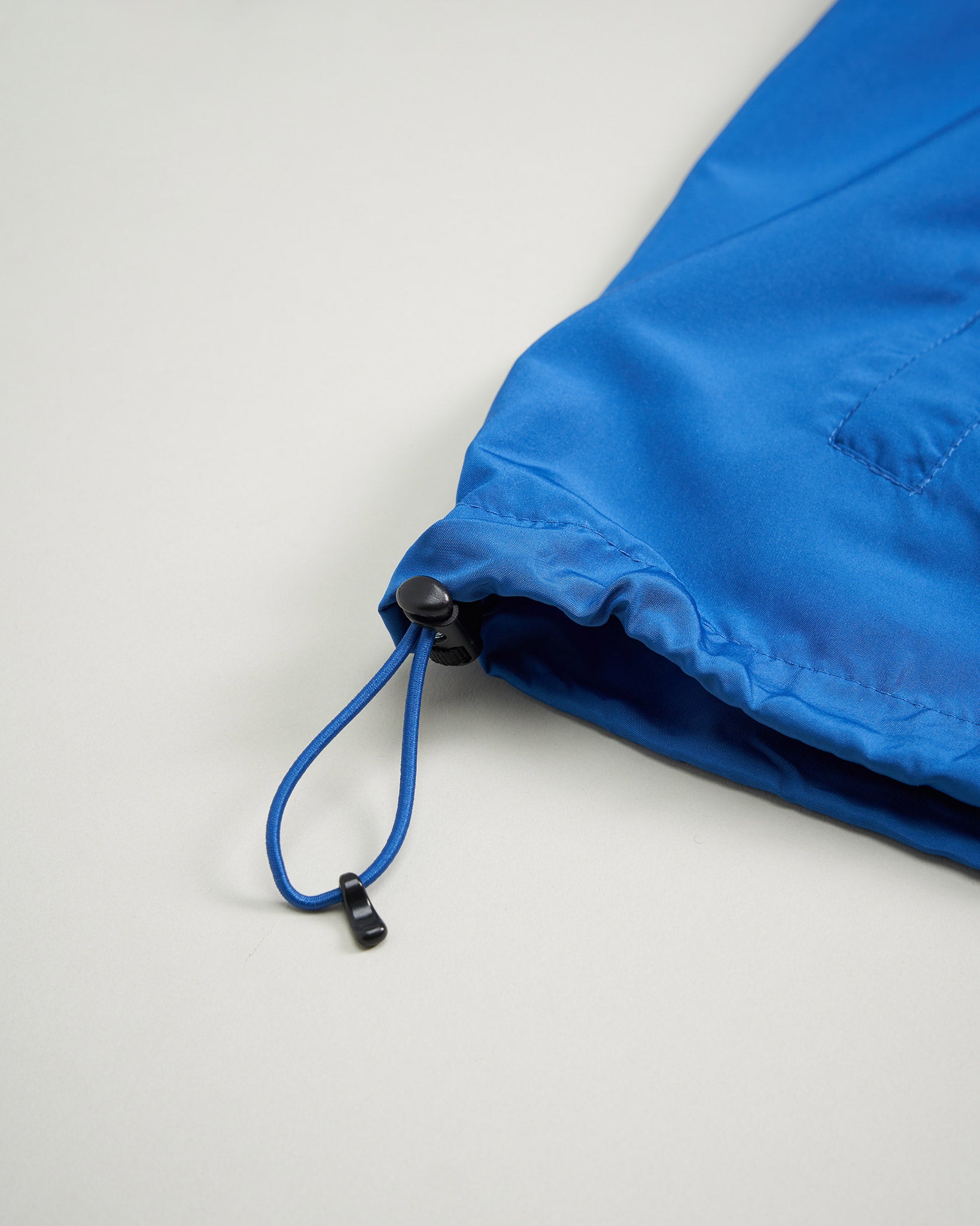 This image displays a close-up of the hemline of a blue garment featuring a drawstring closure highlighting the fabric texture and design details