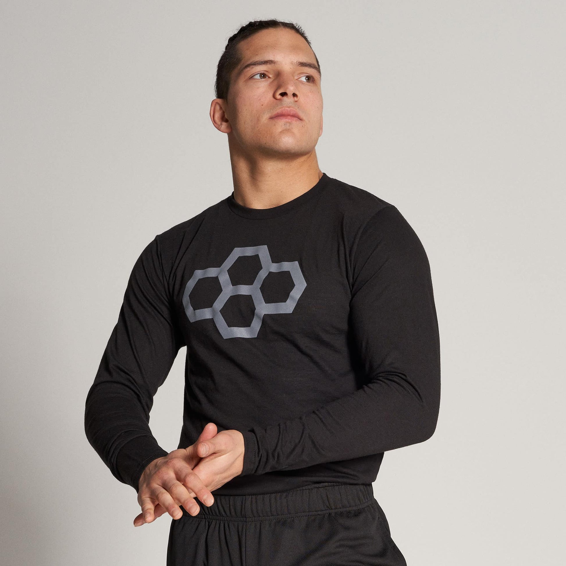 A fit man in a black long-sleeve shirt with a geometric gray design on the chest preparing for physical activity while exuding confidence