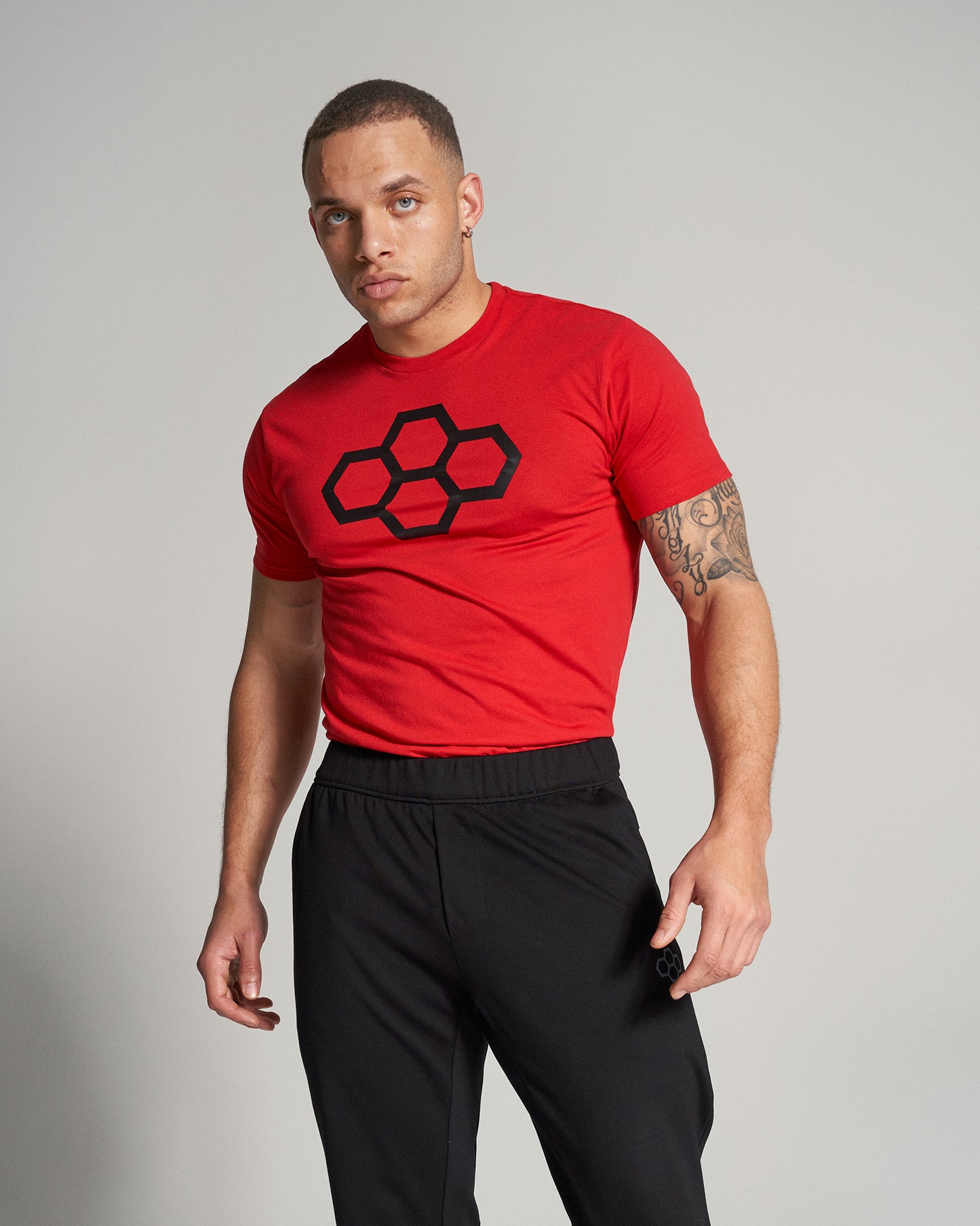 A fit man wearing a red t-shirt with a black graphic design and black athletic pants poses confidently against a light gray background