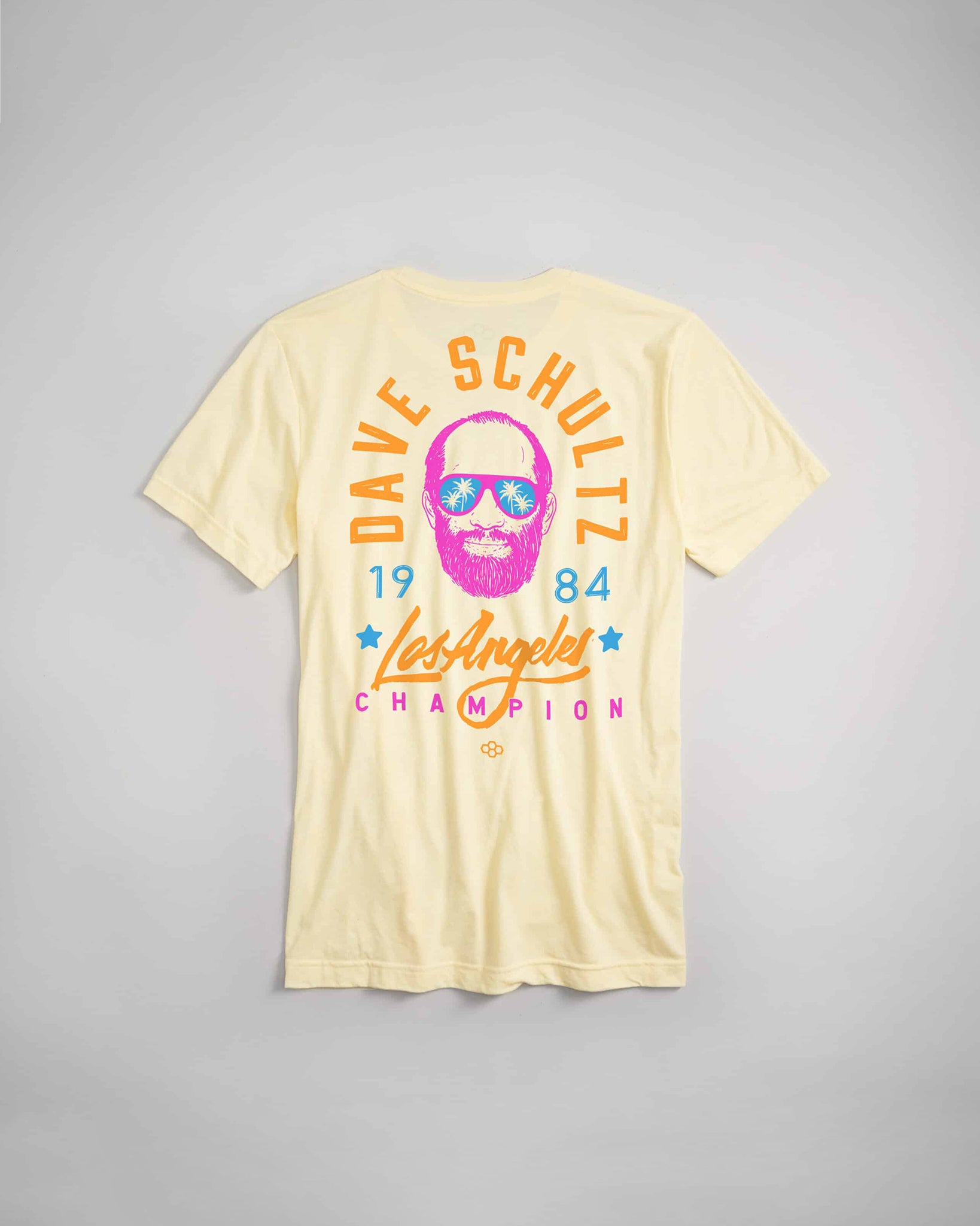 A light yellow t-shirt featuring a vibrant graphic design of a man with sunglasses and a beard along with the text DAVE SCHULTZ 1984 Los Angeles CHAMPION