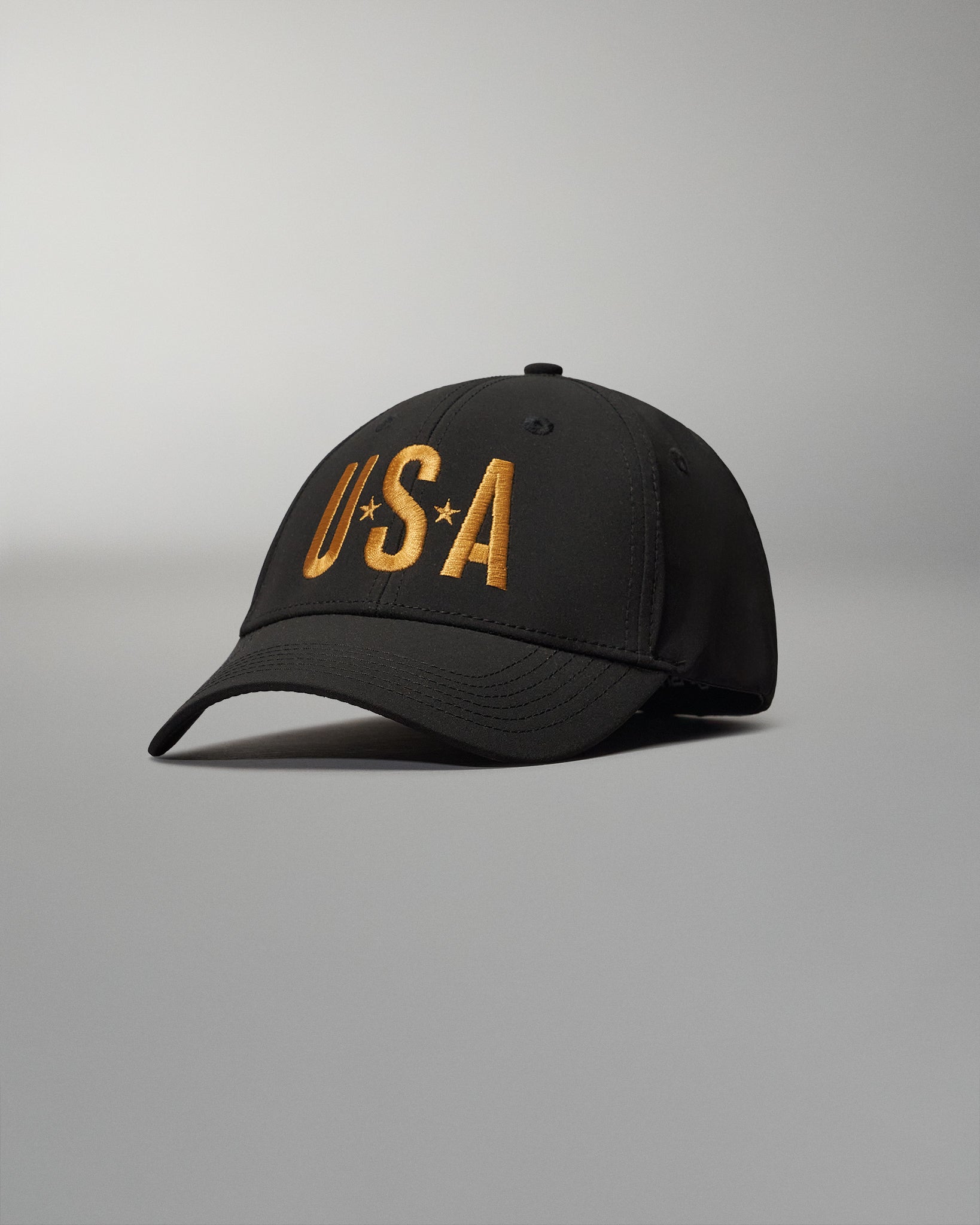 A black cap with bold golden 'USA' lettering is displayed, designed for patriotic wear and featuring a classic silhouette against a muted gray background.