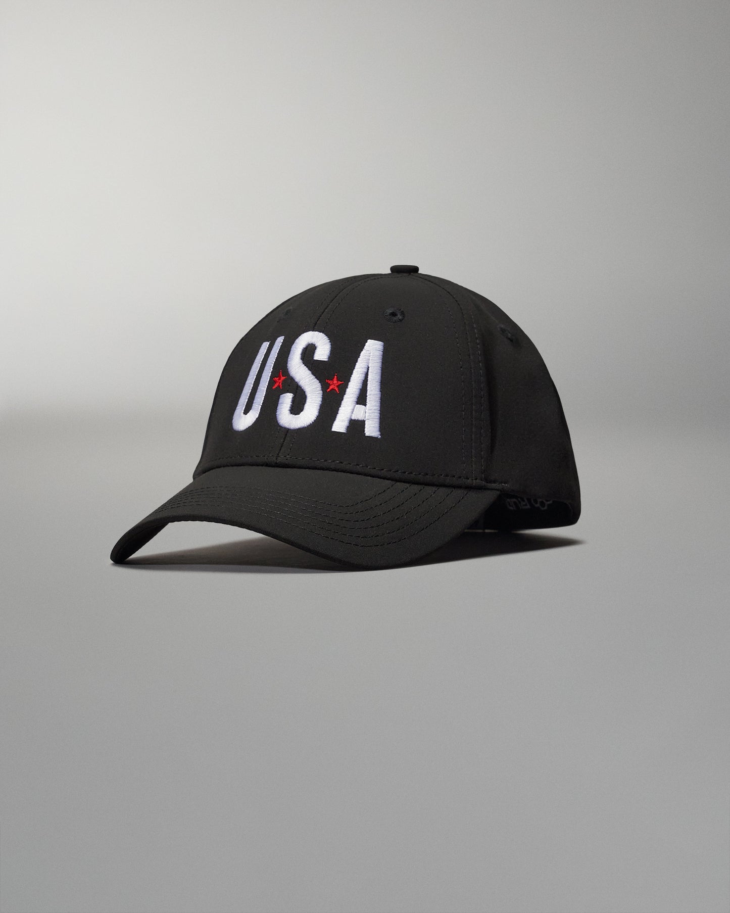 A black baseball cap displays 'USA' in white embroidery with red stars, featuring a structured design and a curved brim against a softly lit background.