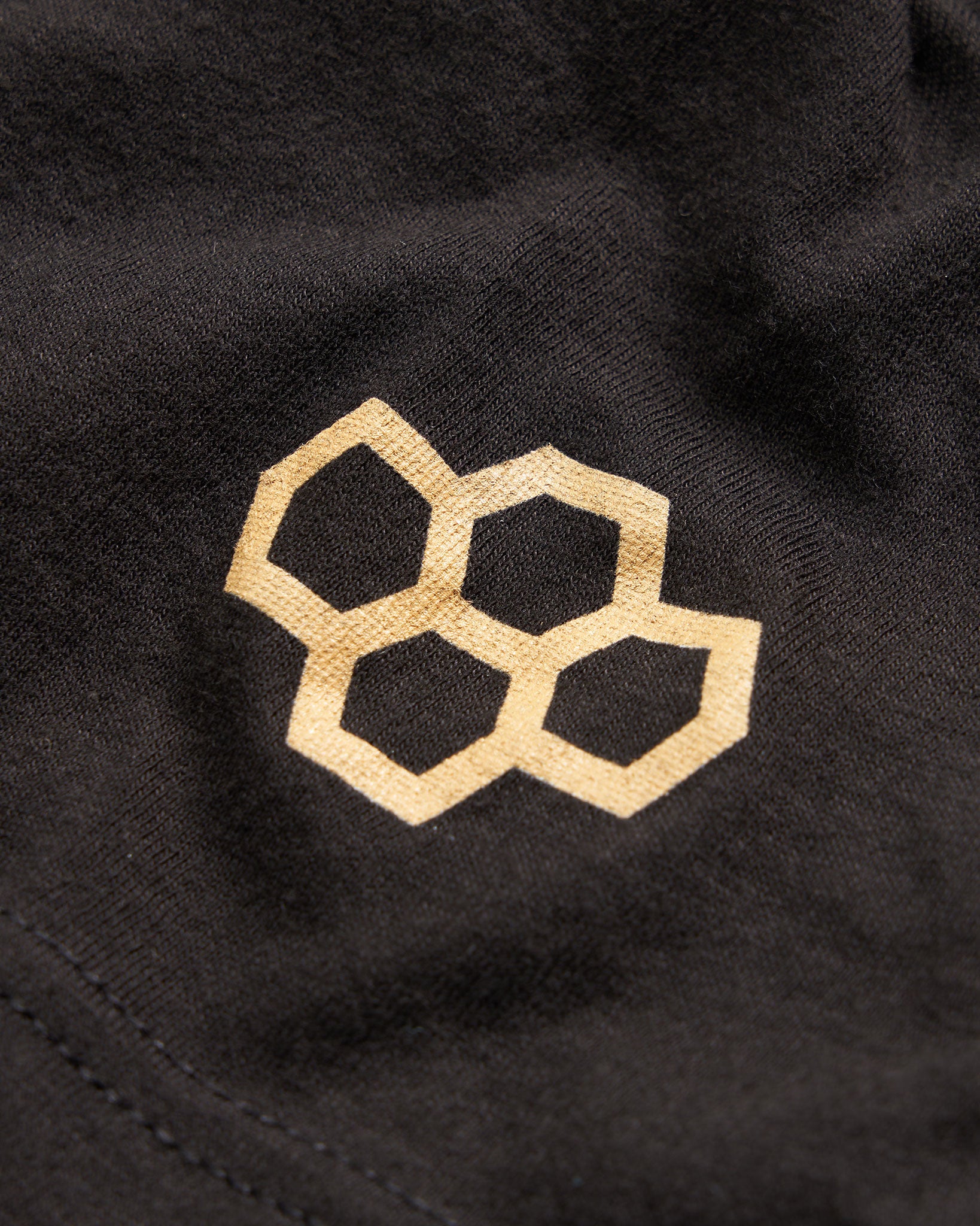 A close-up view of a black fabric featuring a gold honeycomb pattern logo