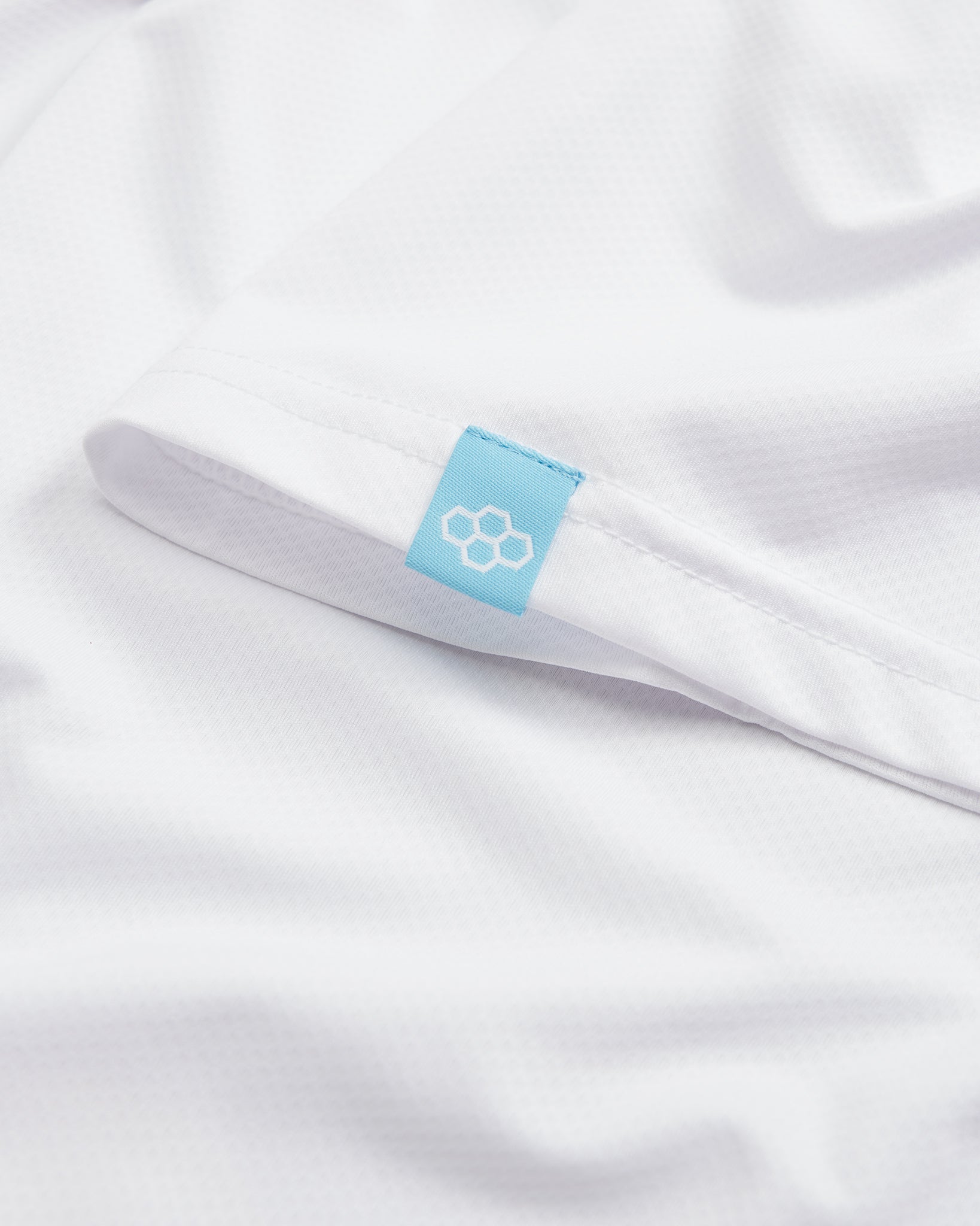 A close-up view of a white athletic shirt featuring a blue label with a hexagonal logo on the sleeve