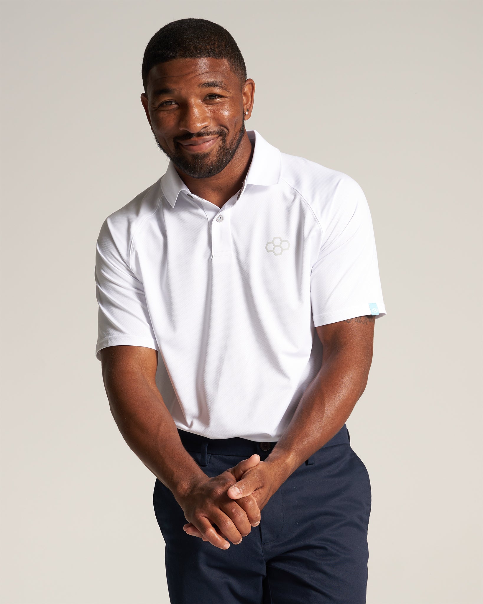 A smiling man in a white polo shirt poses confidently with his hands clasped exuding a friendly and approachable demeanor