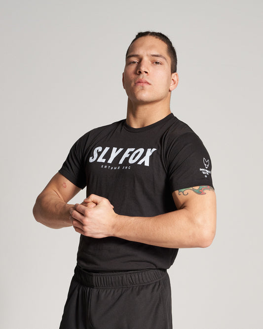 A muscular individual poses confidently in a black SLY FOX branded t-shirt and matching shorts emphasizing a determined expression and athletic physique