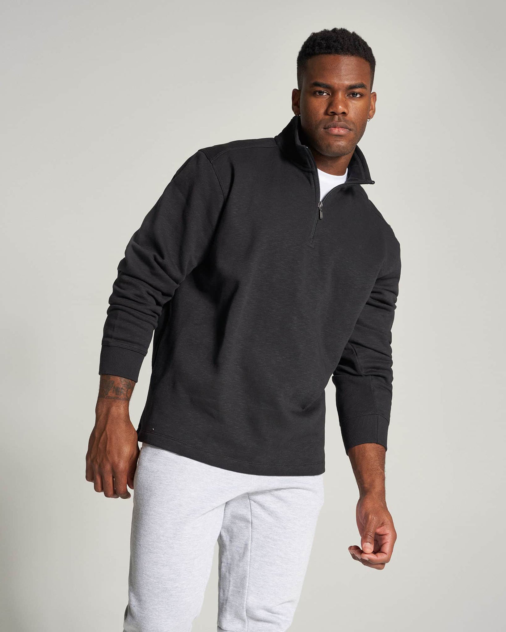 A young man models a stylish black zip-up sweatshirt paired with light gray joggers set against a neutral background that enhances the casual aesthetic