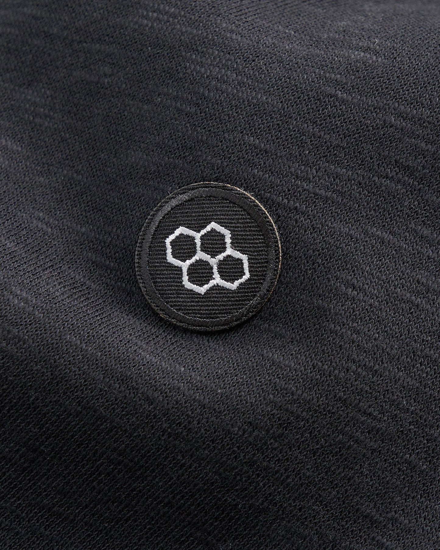 A close-up of a black fabric with a round patch featuring a geometric design of overlapping hexagons in white thread