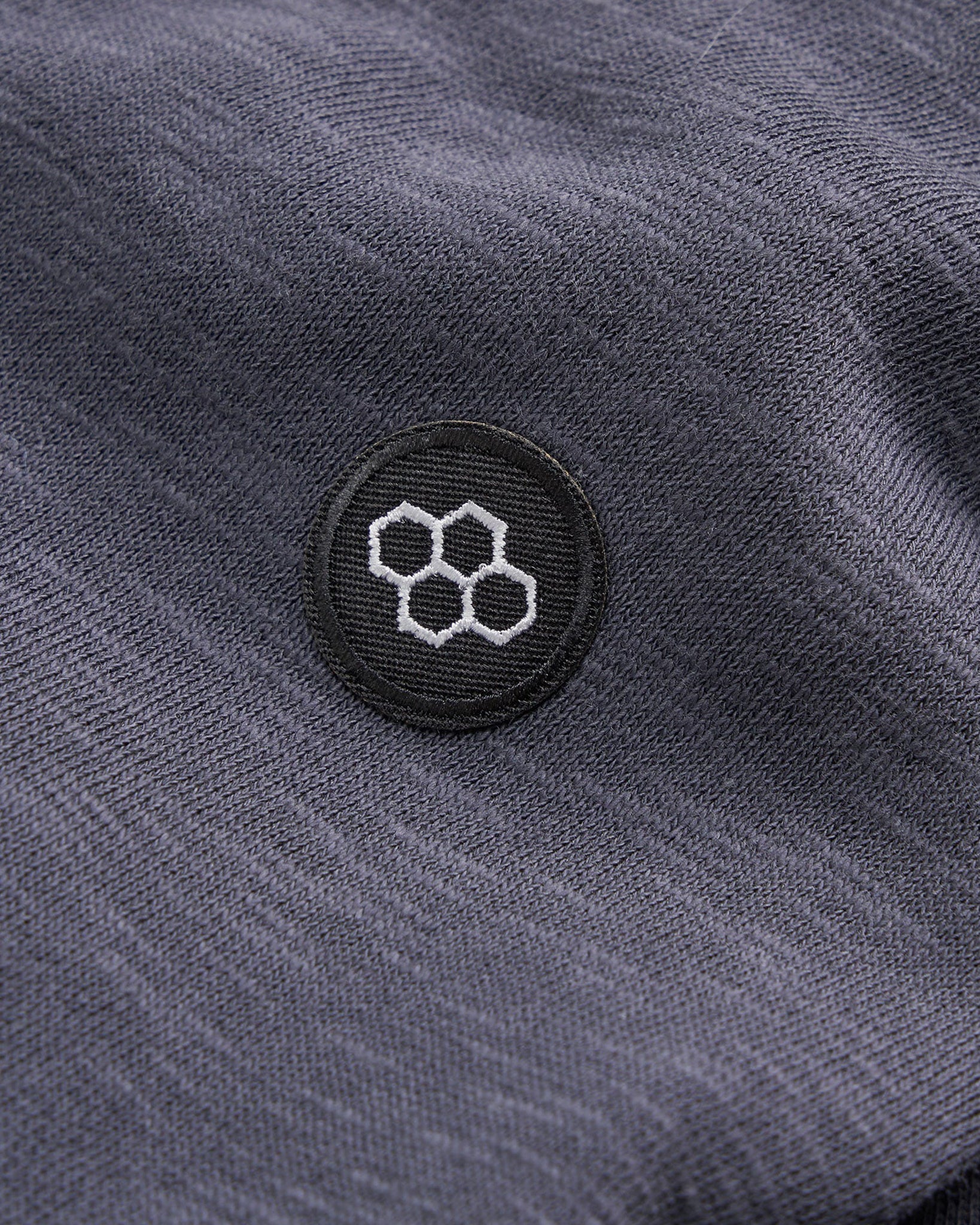 A close-up view of a dark textured fabric featuring a circular embroidered logo with hexagonal shapes in white on a black background