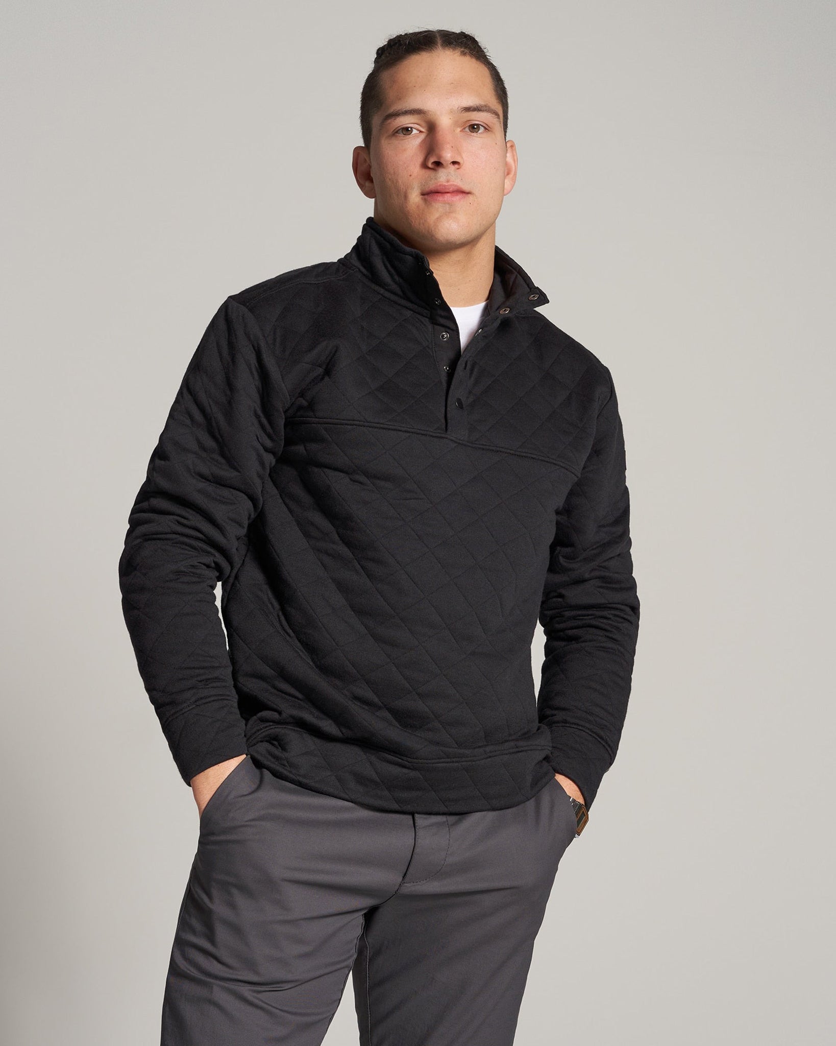 A young man poses confidently in a stylish black quilted pullover paired with gray pants set against a neutral background