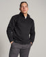 A young man poses confidently in a stylish black quilted pullover paired with gray pants set against a neutral background