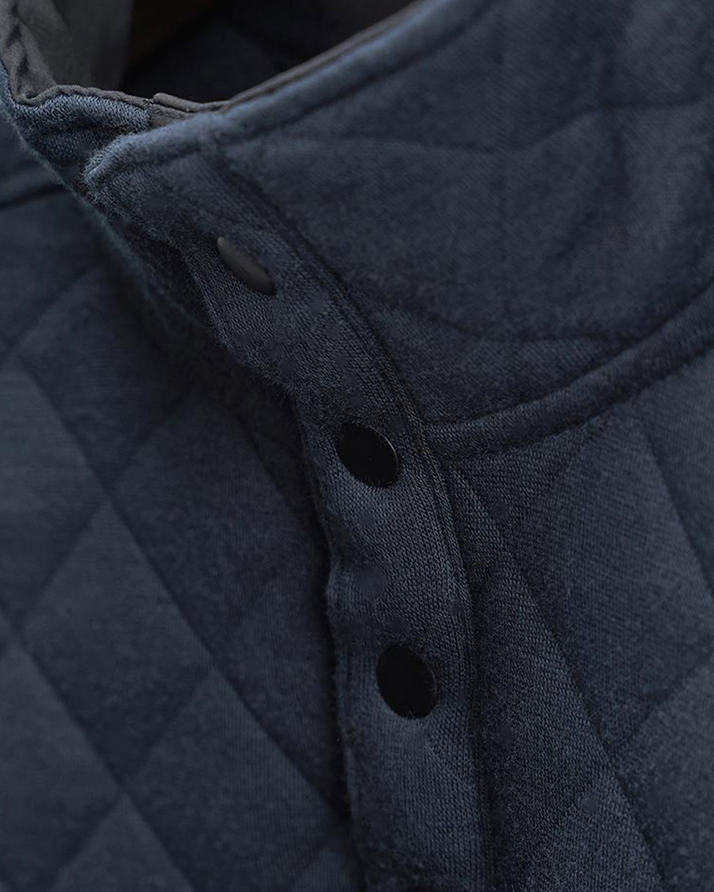 A close-up of a textured dark blue quilted collar featuring black buttons