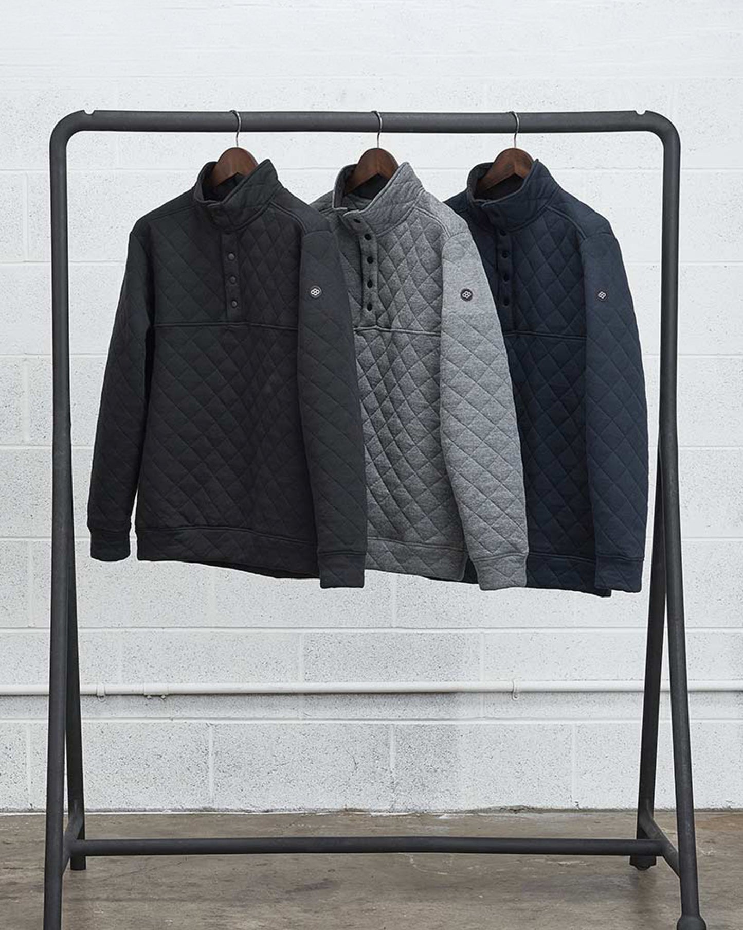 Three quilted pullovers in black gray and navy hanging on a display rack showcasing a stylish and cozy layering option