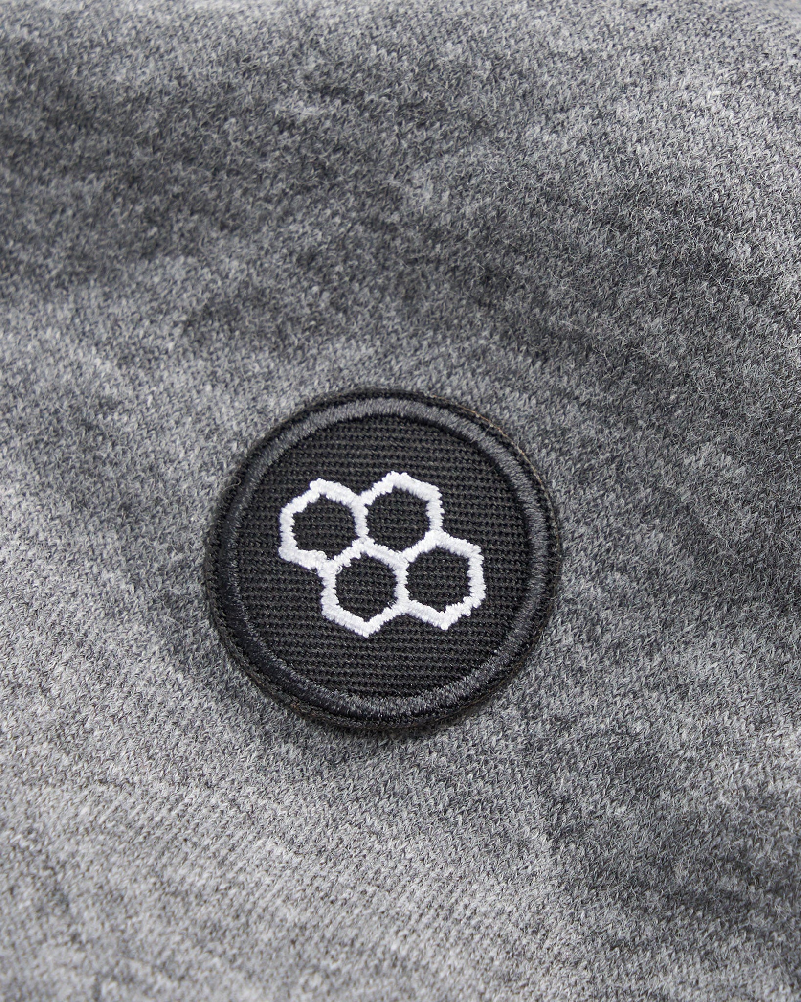 A close-up of a textured gray fabric featuring a black circular patch with a white honeycomb graphic design