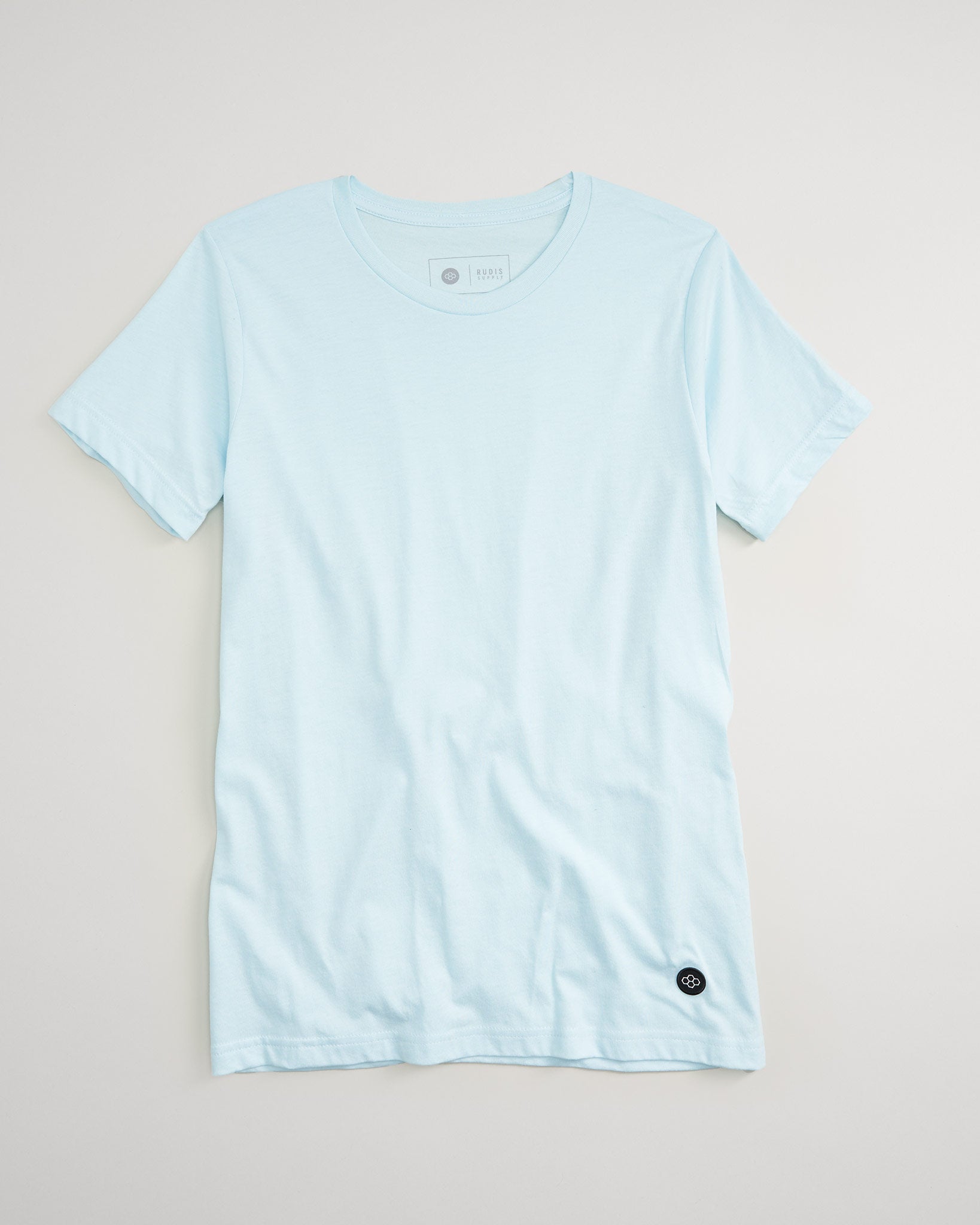 A light blue short-sleeved t-shirt displayed against a neutral background featuring a simple crew neckline and a subtle logo on the bottom left side