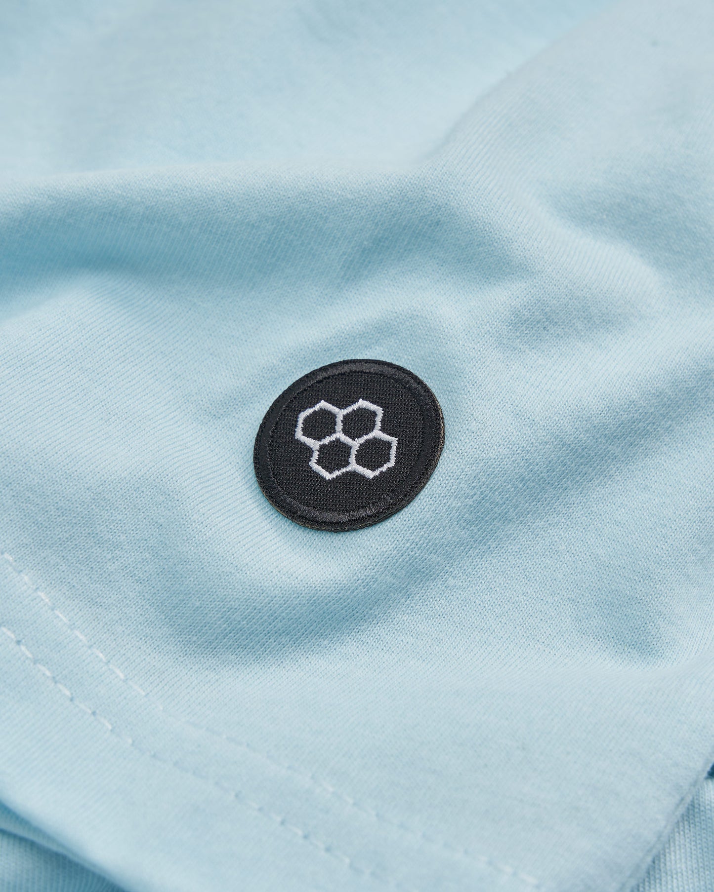 A close-up view of a light blue fabric featuring a black embroidered badge with hexagon designs