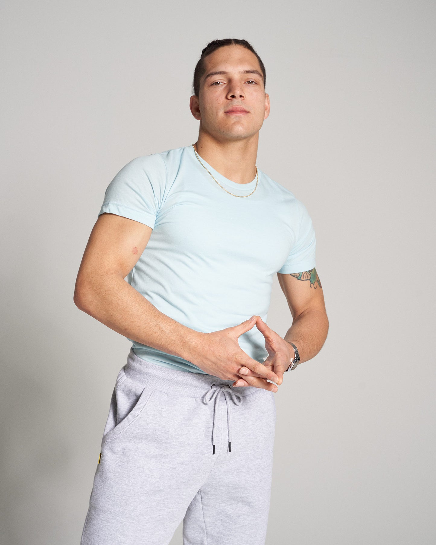 A confident young man poses in a light blue t-shirt and gray sweatpants showcasing a casual yet stylish look