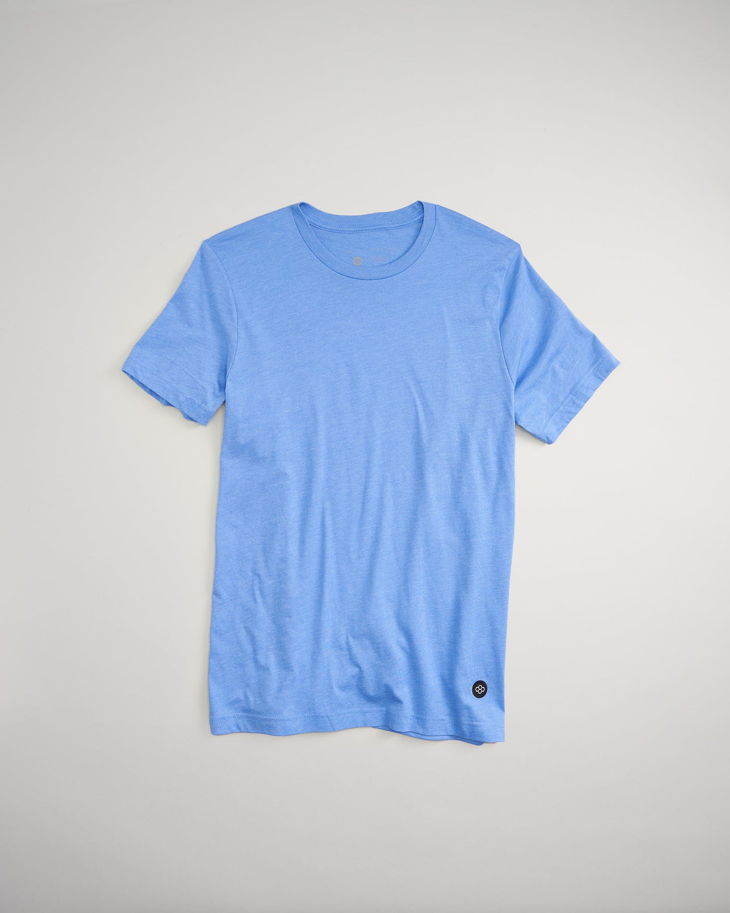 A light blue short-sleeve t-shirt laid flat against a neutral background featuring a minimalistic design with a circular logo at the hem