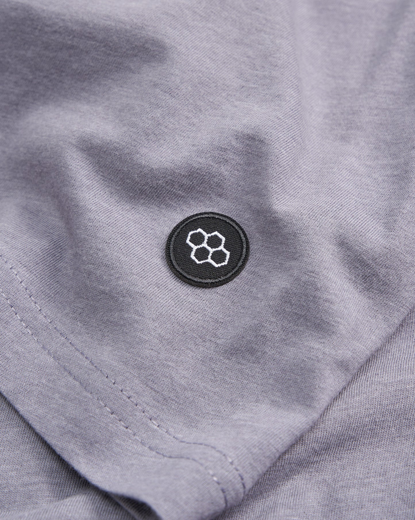 Close-up view of a gray fabric featuring a circular black patch with a geometric logo highlighting the textiles texture and seam details