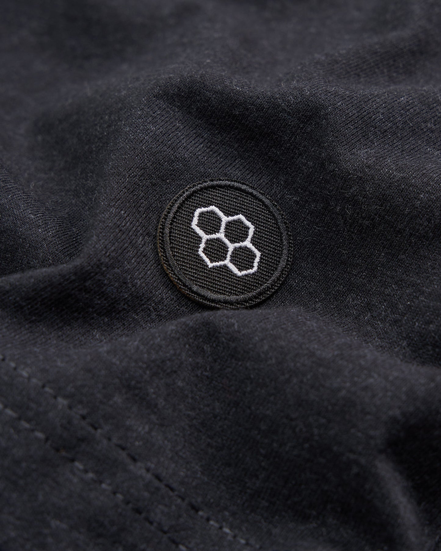 Close-up image of a black fabric featuring a circular embroidered logo with a honeycomb design