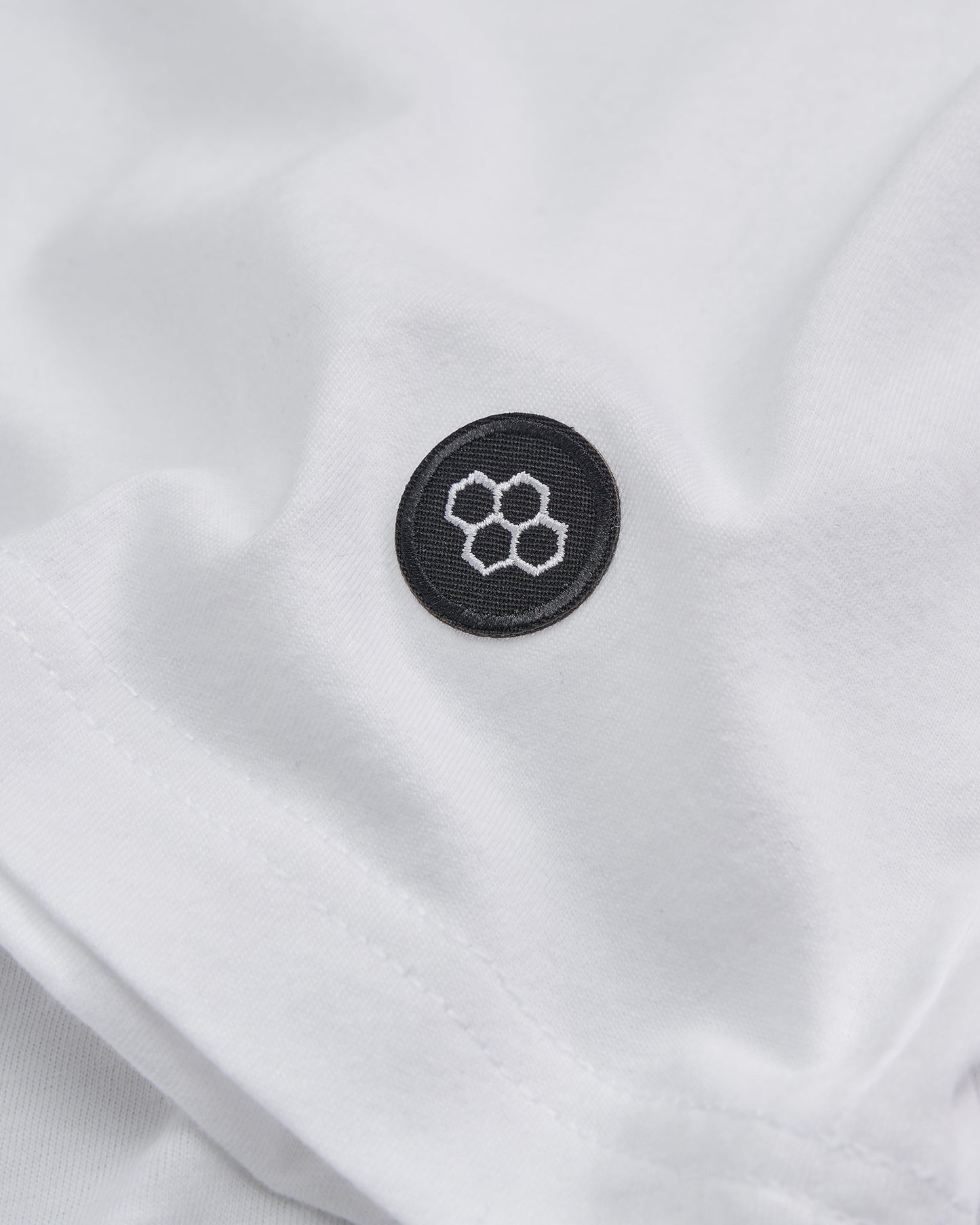 A close-up view of a white garment featuring a round black patch with a hexagonal honeycomb design embroidered in white