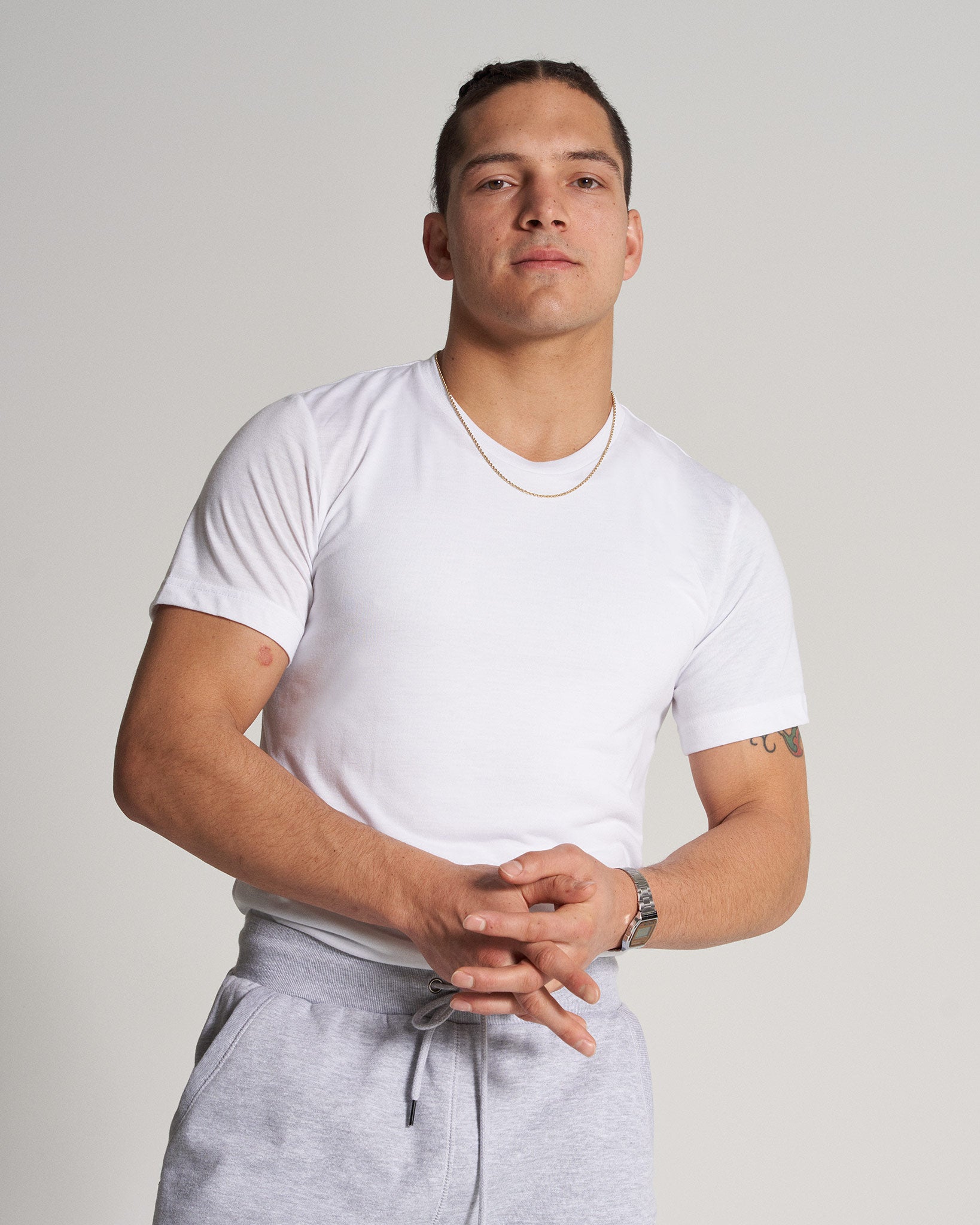 A confident individual stands in a white t-shirt and gray sweatpants showcasing a stylish casual look with a neutral background