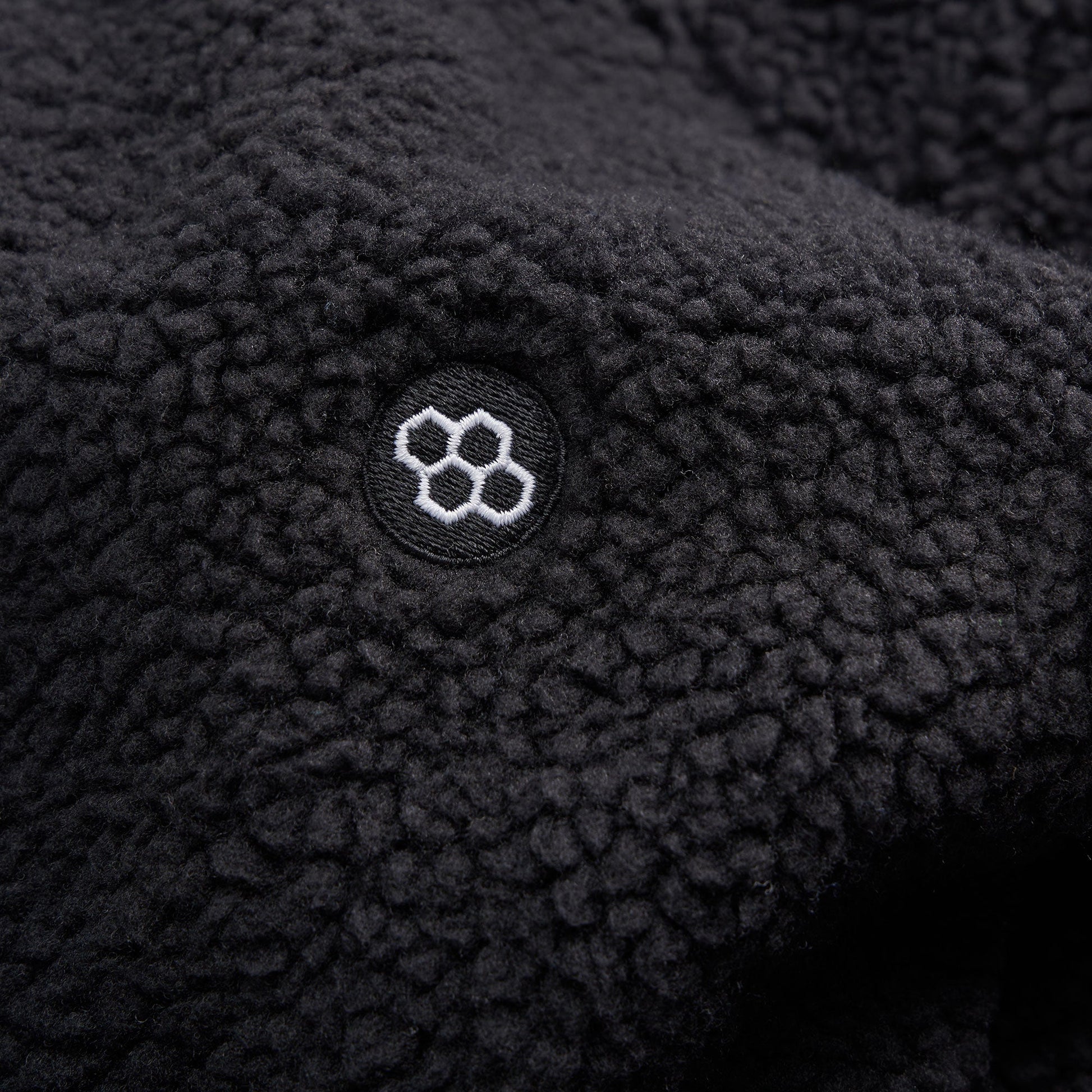 A close-up of a black fleece fabric featuring a circular logo with a honeycomb design embroidered in white