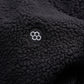 A close-up of a black fleece fabric featuring a circular logo with a honeycomb design embroidered in white