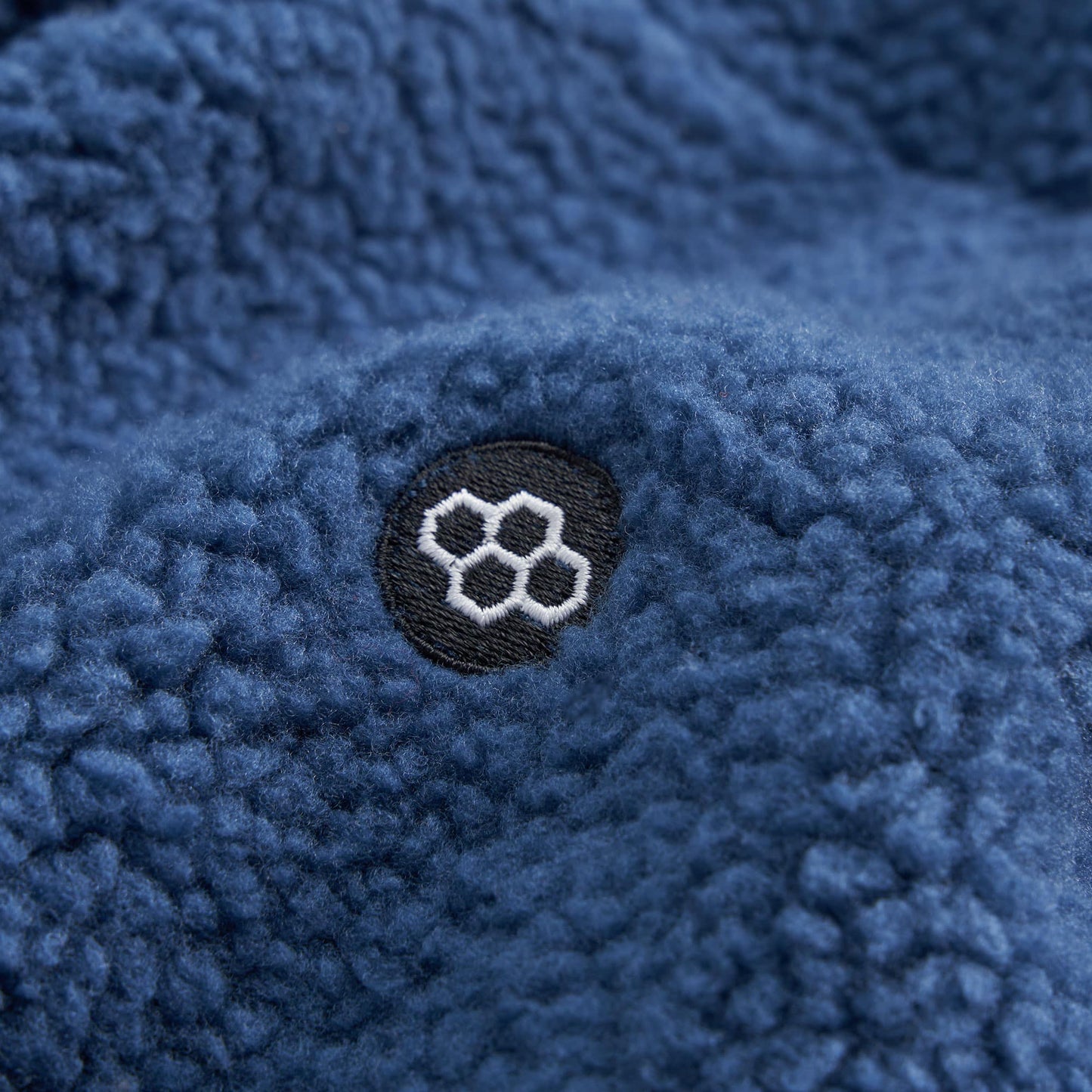 Close-up of a textured blue fleece fabric featuring a circular logo with hexagonal designs in white embroidery