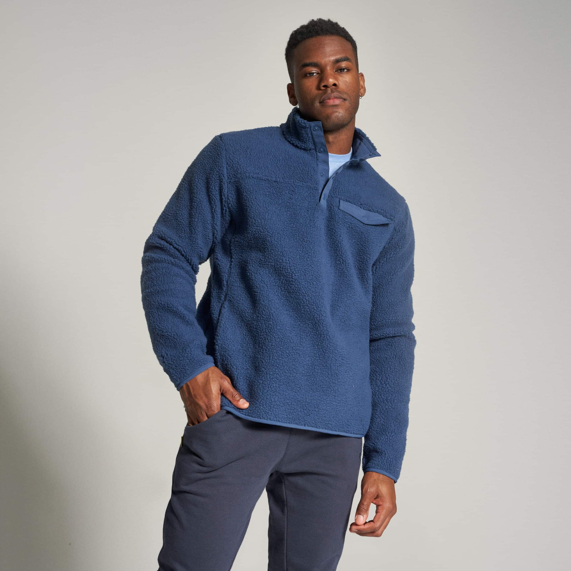 A man wearing a cozy navy blue fleece pullover with a half-zip collar and front pocket paired with dark pants standing confidently in a neutral setting