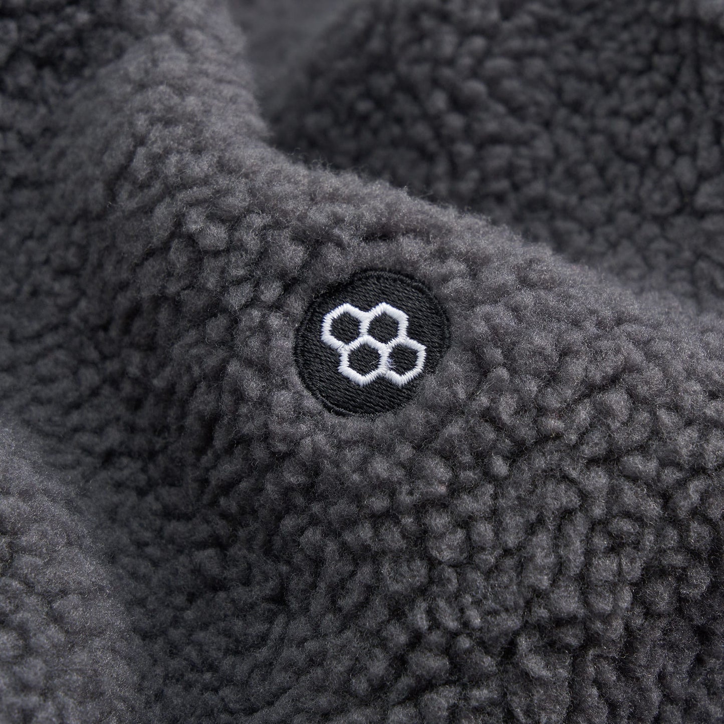 A close-up of soft gray fleece fabric featuring a circular embroidered logo with a hexagonal pattern