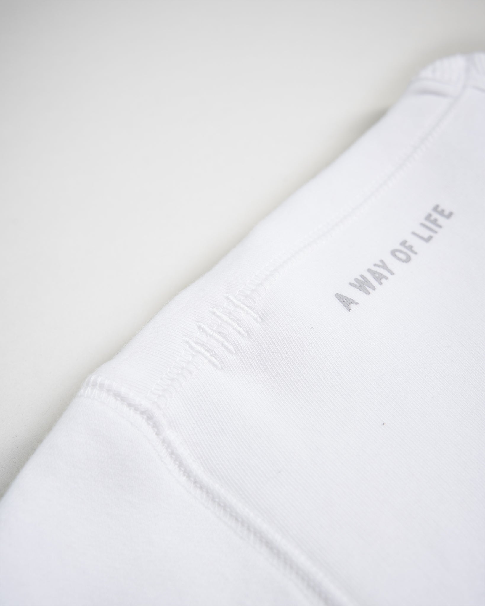 A close-up view of a white garment displaying the phrase A WAY OF LIFE in gray showcasing its texture and seam details