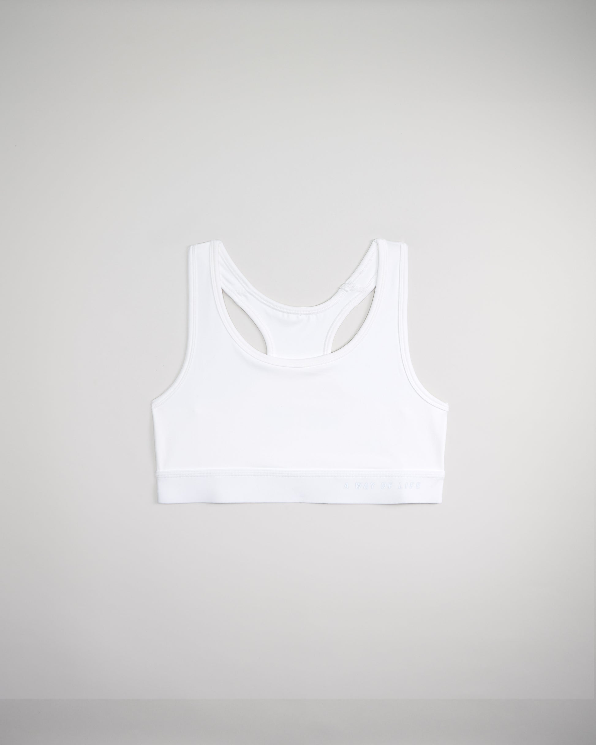 A simple white sports bra featuring a racerback design and a subtle textured band with the phrase A WAY OF LIFE