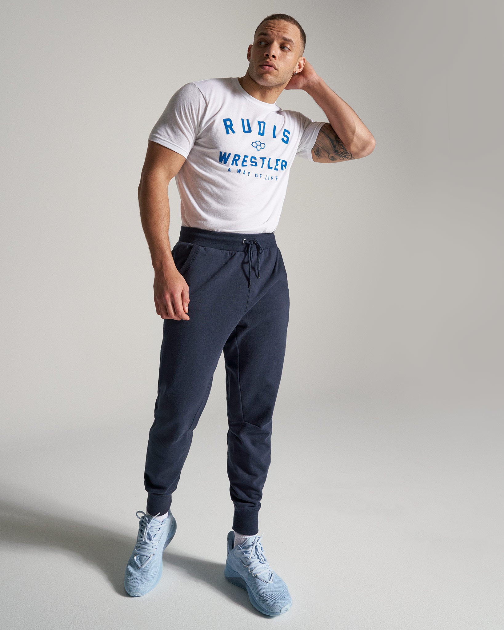 A fit man stands in casual athletic wear featuring a white graphic t-shirt and navy joggers complemented by light blue sneakers