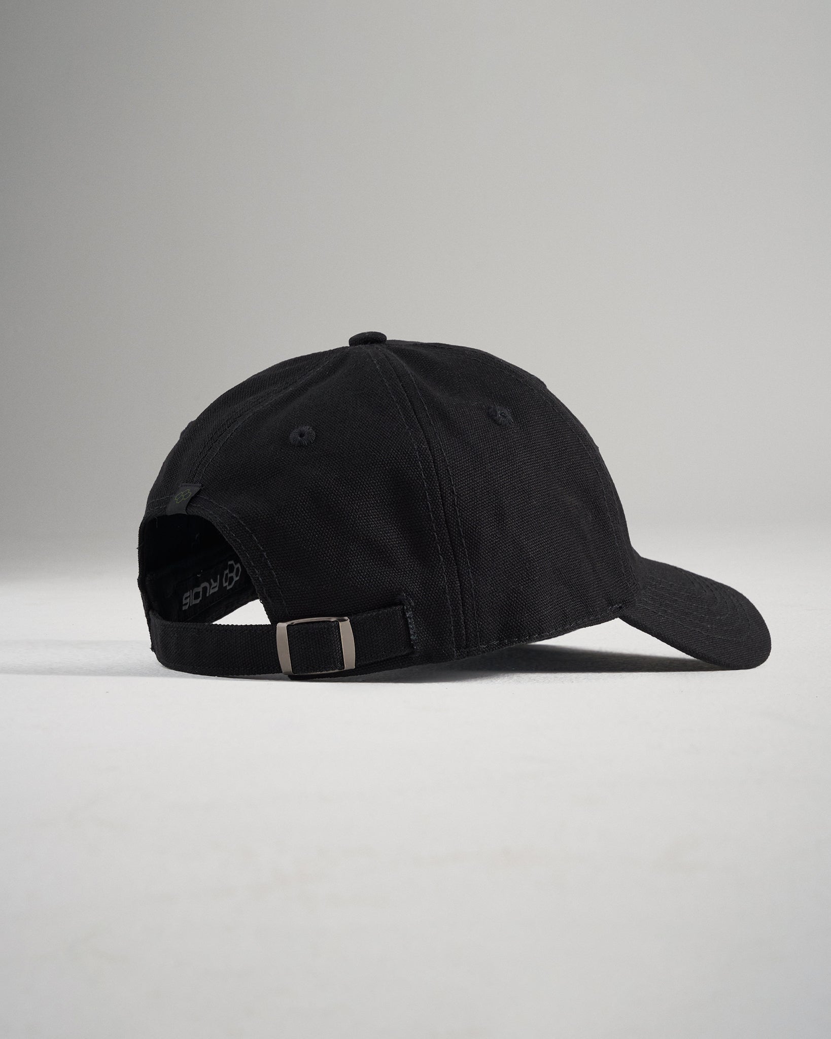 A black baseball cap viewed from the side with a minimalistic design and adjustable strap at the back