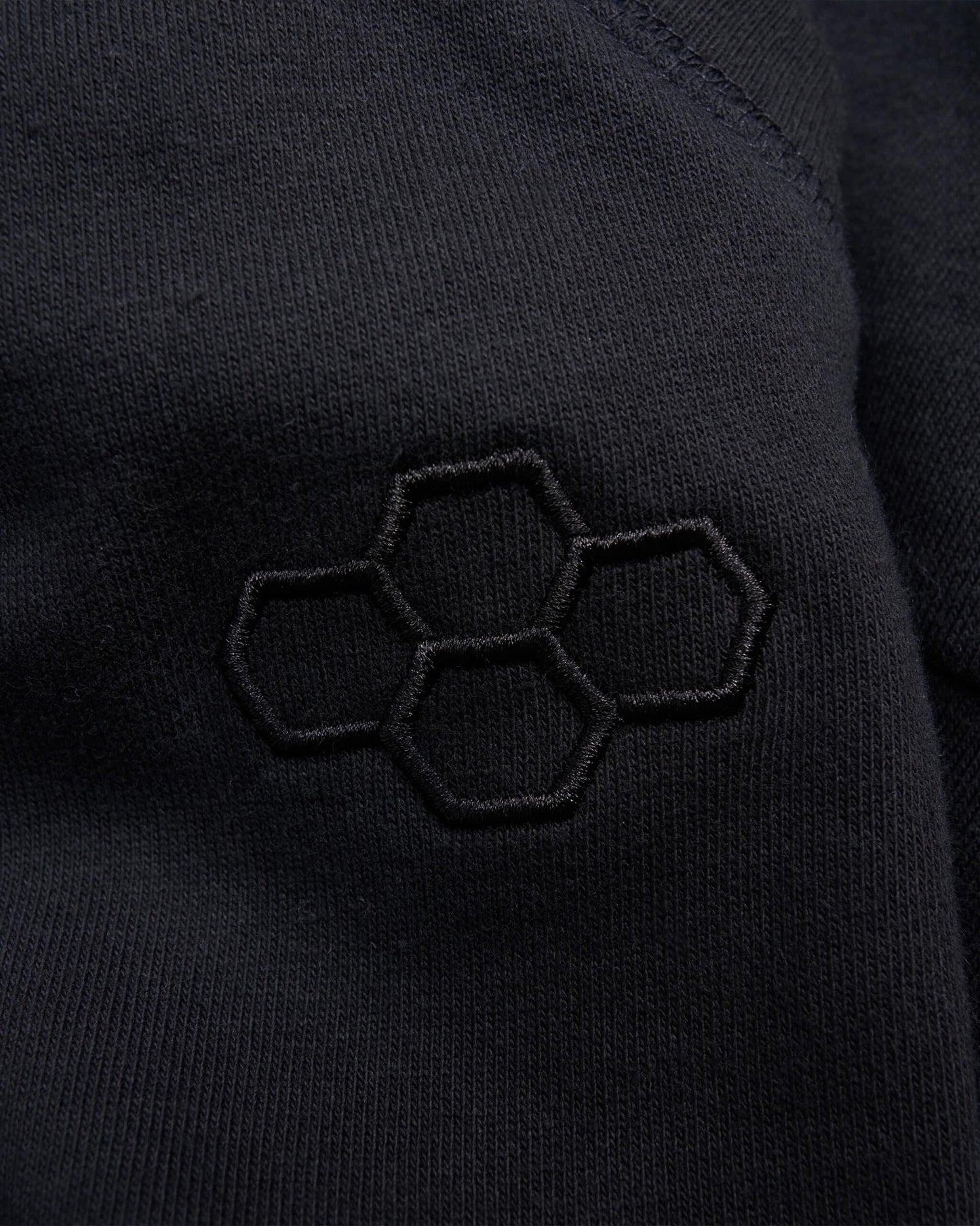 A close-up view of a black fabric featuring an embroidered honeycomb logo on the surface