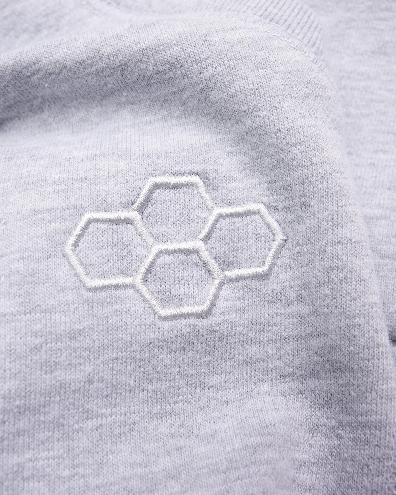 A close-up view of a light gray fabric featuring an embroidered honeycomb design showcasing soft texture and fine detailing