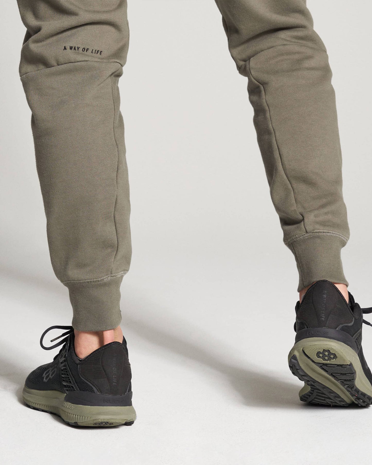 The image features a persons lower body dressed in olive green sweatpants and black athletic shoes emphasizing both comfort and style