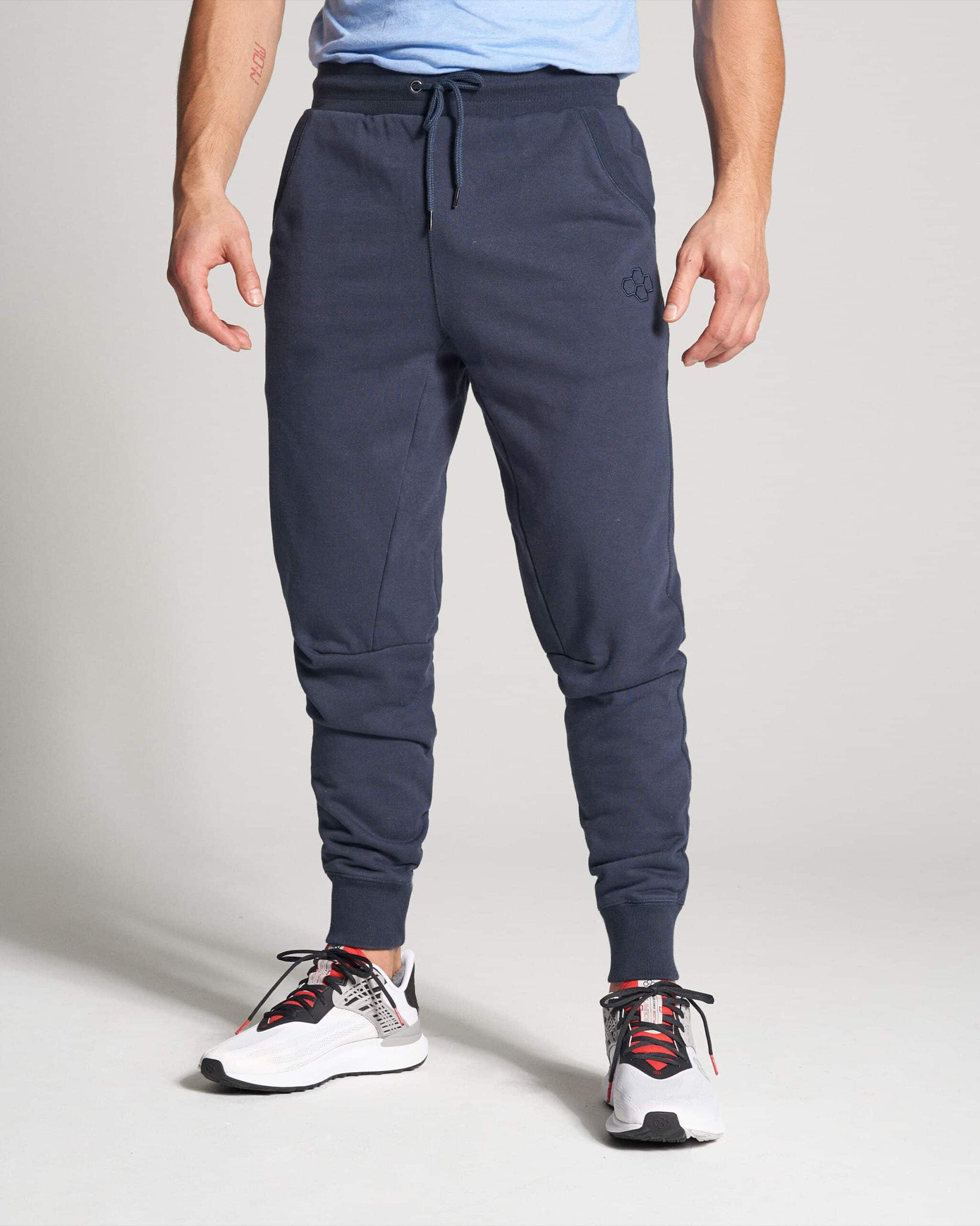 A person wearing navy jogger pants and athletic shoes in a casual pose set against a light background