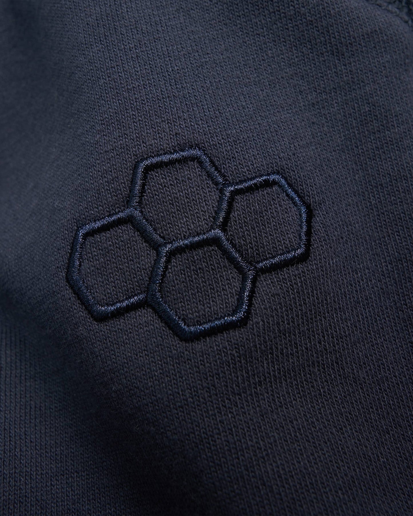 A close-up of a dark fabric featuring a textured embroidery design of interlocking hexagons