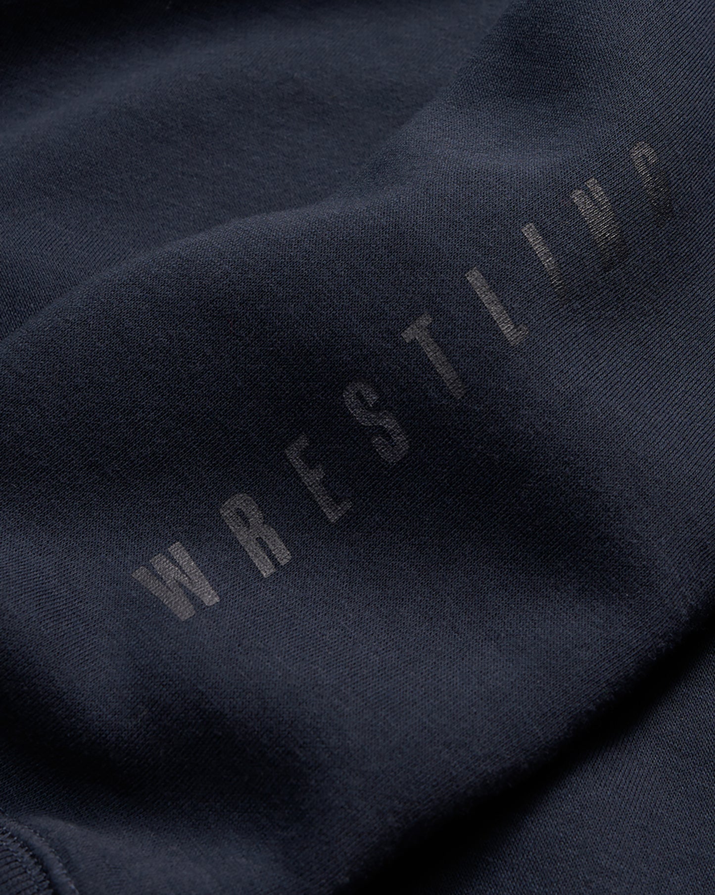 A close-up view of a dark blue fabric featuring the word WRESTLING in subtle large letters